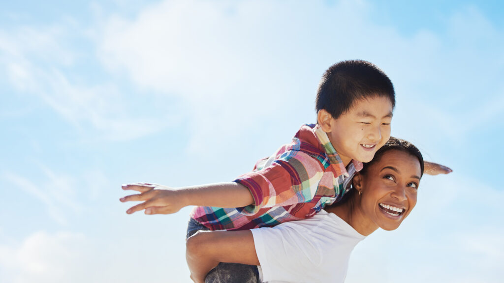 A young boy pretending to fly on the back of a woman, possibly a parental figure